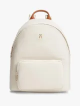Mochila Tommy Hilfiger de nailon color beige, con diseño curvo, bolsillo frontal con cierre y detalles en cuero sintético marrón en el asa superior. Cuenta con el monograma TH metálico dorado en la parte delantera y correas ajustables.