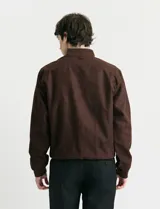 Campera tipo bomber de color marrón, confeccionada en tejido con textura similar a la gamuza, con cierre frontal completo, cuello redondo y puños elásticos.