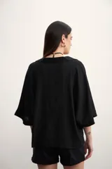 Blusa negra de corte holgado con cuello polo y cierre frontal parcial. Presenta mangas cortas amplias y un diseño minimalista.