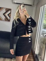 Conjunto de dos piezas tejido al crochet color crudo. Incluye una mini falda de tiro alto y un cardigan corto con mangas largas y lazos para atar en el frente.