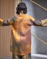 Tapado de lana merino afieltrada color ocre con teñido artesanal tie dye en forma de luna, cierre cruzado asimétrico con broches, cuello alto y bolsillos laterales.