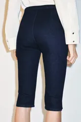 Jeans de tiro medio en denim azul oscuro, con corte capri y pernera entallada. Presenta un diseño con hebilla metálica integrada en la cintura y cierre frontal con cremallera.