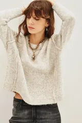 Sweater de punto jaspeado en tono gris claro, con cuello redondo, mangas largas y costuras visibles en el frente. Presenta un corte holgado y ligeramente cropped.