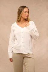 Blusa blanca de manga larga con escote en V y cierre frontal de botones. Presenta detalles de costuras caladas a lo largo del frente y en las mangas.