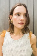 Chaleco de punto color beige con cuello redondo y detalle de plumas en los hombros. Presenta un diseño de espalda irregular y corte al cuerpo.