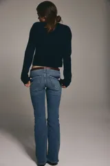 Jeans de denim azul medio con ligero efecto desgastado, tiro bajo y corte acampanado (bootcut) desde la rodilla. Presenta cierre y botón frontal, bolsillos delanteros decorativos y bolsillos abiertos traseros.