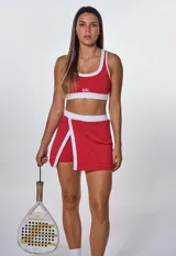 Conjunto deportivo de dos piezas compuesto por un top deportivo con escote redondo y una pollera short con abertura frontal, ambos en color rojo con detalles en blanco.