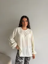 Buzo de viscosa y poliéster color blanco, con textura acanalada, cuello redondo y mangas largas abullonadas con puños elásticos.