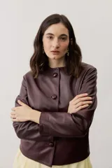 Chaqueta de cuero negra con cuello redondo, cierre frontal de botones forrados y bolsillos ribeteados con detalles de costura decorativa.