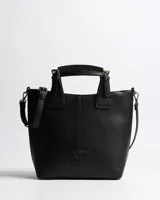 Cartera tipo tote XL Extra Large modelo Fausta, de símil cuero con textura granulada color negro. Cuenta con dos asas de mano, correa bandolera regulable y desmontable, herrajes de metal dorado envejecido y cierre superior. Presenta costura central decorativa y parche con logo en relieve en el frente.