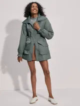 Campera larga color verde con cuello acanalado, cierre de doble sentido, bolsillos de parche grandes, cintura interior ajustable y puños con borde con volados.