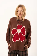 Buzo de punto color chocolate con diseño de flor grande en el frente en tonos rojos y centro texturizado en color crema. Presenta cuello redondo, mangas largas y puños y ruedo acanalados.