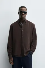 Camisa de corte regular fit confeccionada en tejido de algodón con textura de cuadrillé. Presenta cuello solapa, manga larga con puños abotonados y cierre frontal mediante botonadura.