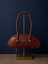 Cartera estilo baguette de cuero con textura tipo reptil, color marrón. Presenta una silueta alargada y estructurada, con manijas largas y detalles de nudos esféricos metálicos en la unión de las mismas. Incluye placa metálica con logo de la marca en el frente.