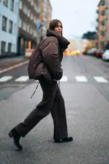 Anorak corto acolchado color marrón chocolate, con cuello subido, manga larga con puños elásticos y cierre frontal con botones ocultos y lazada lateral.