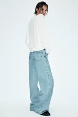 Jeans de tiro alto con diseño wide leg y cinco bolsillos. Presenta cierre frontal con cremallera y botón, e incluye un cinturón a contraste con hebilla metálica.