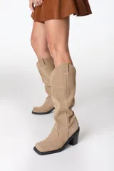 Bota de caña alta color beige, de cuero gamuzado, con taco cuadrado y punta cuadrada.