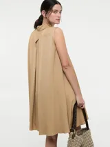 Vestido camisero corto color beige, sin mangas, con cuello clásico, cierre frontal con botones y bolsillos laterales.