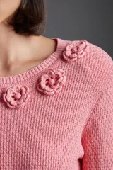 Sweater de punto color rosa con cuello redondo y apliques de flores en el escote.