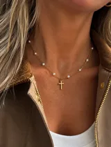 Gargantilla de acero dorado con cadena de eslabones intercalados con pequeñas perlas sintéticas y un dije colgante en forma de cruz.