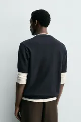 Remera de punto de algodón color negro, con cuello panadero y cierre frontal de tres botones, mangas cortas y acabados en rib.