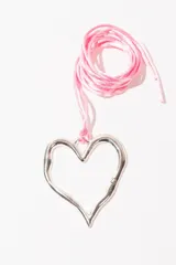 Collar con dije plateado en forma de corazón abierto, con detalle de pequeño corazón en una de las puntas. Cordón fino color rosa.