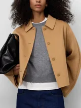 Chaqueta corta color camel con cuello solapa, manga larga japonesa y cierre frontal con botones. Presenta un diseño con capa superpuesta en la espalda.