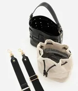 Cartera bucket Satinato de color negro, confeccionada en PU con diseño trenzado y costuras a la vista en color blanco. Cuenta con un compartimento interno de tejido color beige con cierre de cordón ajustable, asa corta superior y una correa larga ancha desmontable de color negro. Los herrajes son de metal dorado.