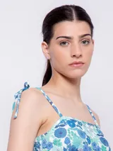 Top corto con escote recto y tirantes finos ajustables mediante nudo en los hombros. Presenta un estampado floral sobre fondo oscuro, con flores rosadas y hojas turquesas.