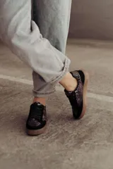 Zapatillas negras con paneles laterales de efecto piel de serpiente metalizado en tonos bronce y negro. Tienen cordones negros y suela de goma color caramelo.