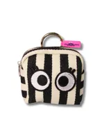 Billetera pequeña tipo monedero con diseño de rayas verticales en blanco y negro, decorada con dos ojos grandes bordados con pestañas. Incluye una argolla metálica para colgar y una etiqueta de silicona rosa con logo.
