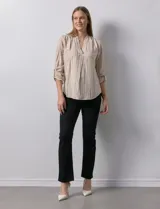 Blusa de manga larga con escote en V, confeccionada en tejido ligero con estampado de rayas verticales en tonos beige y blanco. Presenta un diseño con pliegue frontal y mangas ajustables mediante presilla y botón.