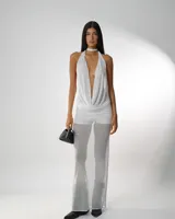 Vestido blanco de microtul premium, con escote halter profundo y drapeado en el busto. La prenda es ajustada en la parte superior y presenta un pantalón ancho y transparente debajo.