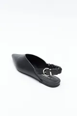 Zapato destalonado de punta fina, color negro, con base baja y tira trasera elástica con hebilla metálica ajustable. Diseño minimalista.