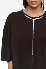 Remera corta de corte boxy y color negro, con escote redondo, mangas cortas y aplicación de lentejuelas en el contorno del cuello y formando una línea vertical central.