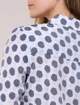 Camisa de gasa blanca con estampado de lunares en tonos azules, cuello con solapa, cierre frontal de botones, bolsillo aplicado en el pecho y detalle de nudo en el dobladillo inferior. Cuenta con mangas largas regulables.