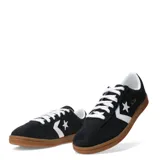 Championes Converse All Star de corte bajo, confeccionados en gamuza negra con el icónico logo de estrella y chevrón en blanco en el lateral. Presentan cordones blancos, interior acolchado y suela de goma color caramelo.