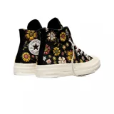 Championes Converse modelo Chuck 70 de caña alta, con diseño estampado de flores en tonos amarillos, rosas y verdes sobre base negra. Presenta el parche clásico de la marca en el lateral, puntera de goma y suela de plataforma en color crema.