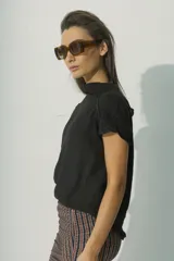 Blusa de lino color negro, con cuello alto y mangas cortas con detalle de costura decorativa en los hombros. Presenta un diseño minimalista de silueta recta y tejido liviano.