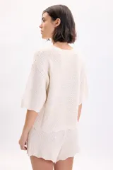 Sweater color crudo de manga corta, confeccionado en tejido de punto con diseño de textura fantasía, cuello redondo y corte holgado.