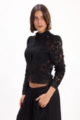 Blusa corta de encaje negro con cuello alto, mangas largas abullonadas y cierre frontal con nudos o botones chinos tradicionales.