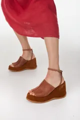 Sandalia de plataforma corrida de cuero marrón, con capellada ancha y tira fina ajustable al tobillo con hebilla metálica.