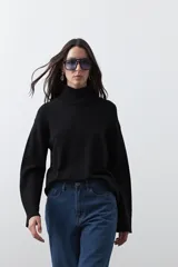 Polera de tejido liviano en color negro, con cuello alto, mangas largas y corte relajado. Presenta un diseño minimalista con recortes laterales que aportan estructura a la prenda.