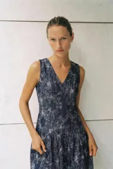 Vestido corto sin mangas de color azul marino, con escote en V y bordados florales a contraste. Presenta un diseño ajustado con corte en la cintura y falda con volante en el bajo. Cuenta con cierre de cremallera en la espalda.