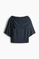 Top corto de punto elástico de viscosa color gris oscuro, con escote bote, hombros caídos y mangas cortas amplias. Cuenta con una sección superior superpuesta con diseño asimétrico efecto capa.