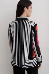 Camisa de manga larga con cuello solapa y cierre frontal de botones. Presenta un diseño estampado con bloques geométricos en tonos azul, blanco y negro.