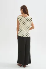 Top de poliéster negro con estampado de lunares blancos, diseño al cuerpo y cuello asimétrico de manga corta.