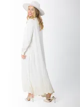 Maxi vestido camisero de lino blanco con bordados en tono beige en mangas y ruedo. Presenta cuello camisero, botones frontales y mangas largas.