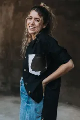 Camisa color naranja de lino o algodón con cuello clásico, cierre frontal con botones y mangas largas con puños abotonados. Presenta un bolsillo de cuero marrón en el pecho.