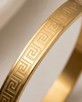 Esclava rígida de acero con baño de oro, con diseño de guarda griega grabado en toda su superficie.